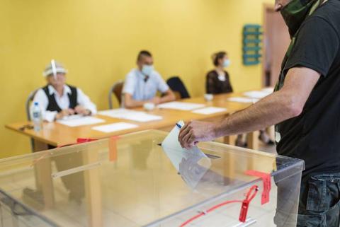 Un votante depositando su voto en una urna mientras se observa a otras personas en un proceso electoral.