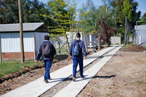 Dos personas caminan por una vereda junto a una construcción.