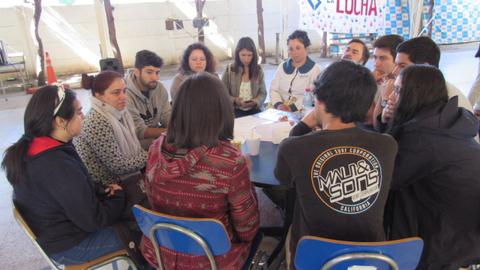 Un grupo de jóvenes sentados alrededor de una mesa, conversando en un ambiente informal.