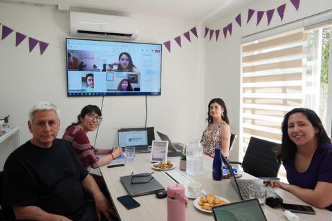 Un grupo de personas participa en una reunión híbrida en una sala con pantallas y comida.