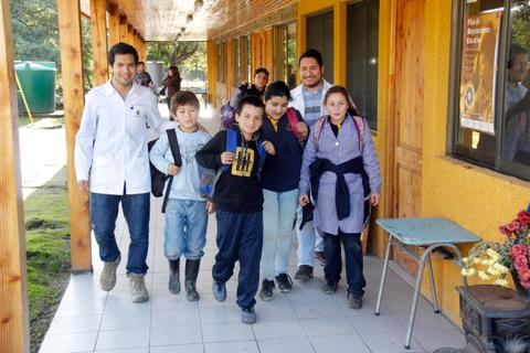 Un grupo de niños y adultos caminan por un pasillo exterior de una escuela.