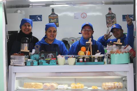 Un grupo de cuatro personas sonrientes detrás de un mostrador lleno de alimentos y bebidas.