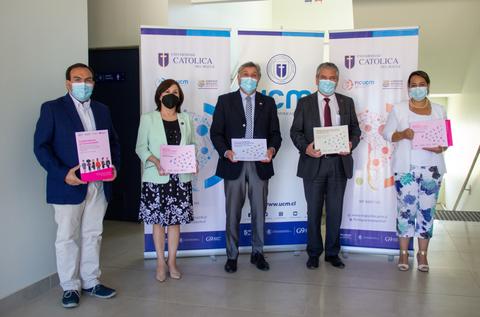 Un grupo de cinco personas sostiene documentos frente a un fondo con el logo de la universidad.