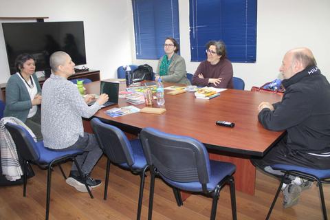 Un grupo de cinco personas se reúne en una sala de trabajo, conversando alrededor de una mesa.
