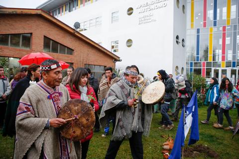 Una ceremonia cultural con personas tocando tambores y vistiendo vestimenta tradicional en un ambiente comunitario.