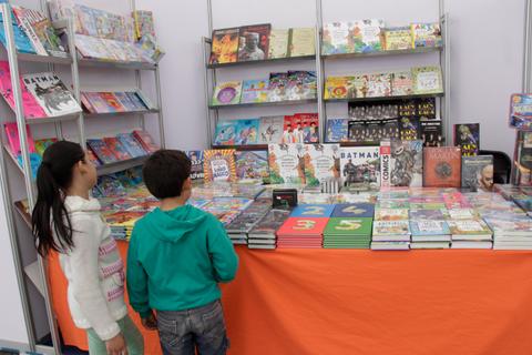 Dos niños observan un expositor lleno de libros en una feria.
