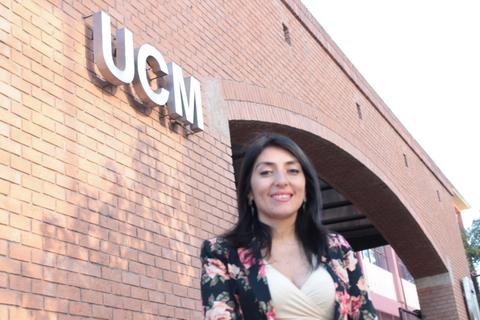 Mujer sonriente de pie frente a un edificio con la sigla UCM.