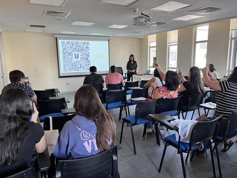 Una presentación en un salón con asistentes usando sus celulares para captar información.