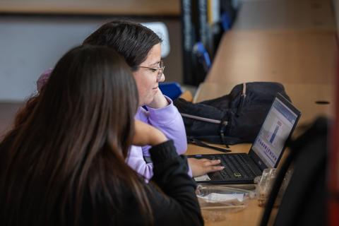 Dos jóvenes están trabajando en una computadora portátil en un ambiente académico.