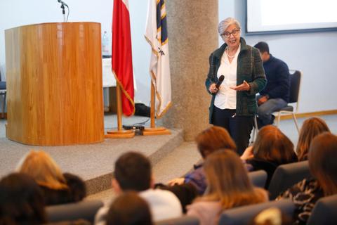 Una mujer está dando una charla frente a un público sentado en un auditorio.
