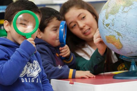 Niños observando un globo terráqueo con lupas bajo la guía de una mujer.