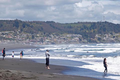 Una playa con varias personas caminando y olas rompiendo en la orilla.