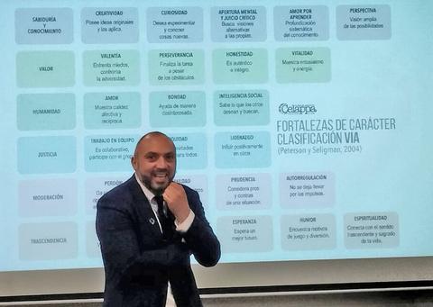 Un presentador explica las fortalezas de carácter clasificadas en un esquema visible detrás de él.