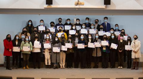 Un grupo de personas posando en un auditorio, cada una sosteniendo un certificado.