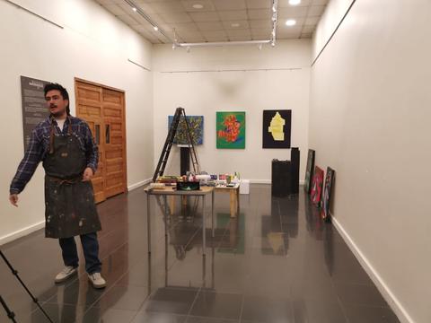 Un artista se encuentra en una galería de arte con varias obras expuestas en las paredes.