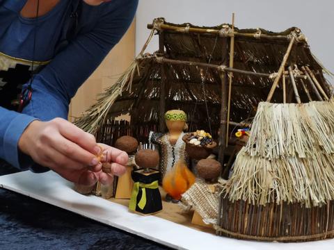 Una persona está trabajando en una maqueta de una escena con cabañas de paja y figuras decorativas.
