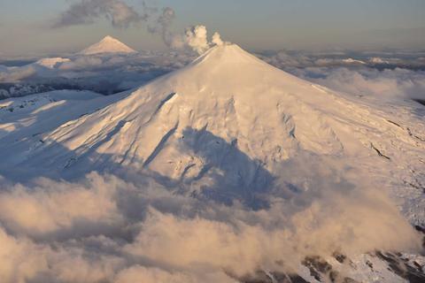 Un paisaje montañoso con volcanes cubiertos de nieve y nubes en el cielo.