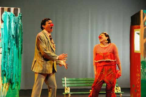Dos actores de un espectáculo teatral actúan con trajes de payaso en un escenario colorido.