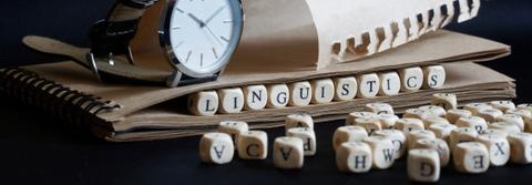 Se observa un reloj y un cuaderno junto a bloques de letras que forman la palabra 'LINGUISTICS'.