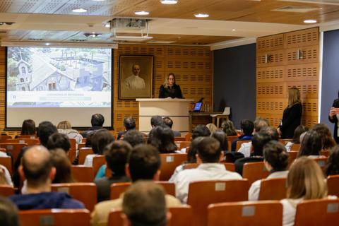 Una presentación en un auditorio con una oradora en el podio y una audiencia atenta.