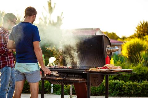 Dos hombres cocinando a la parrilla al aire libre durante un día soleado.