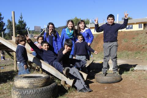 Un grupo de niños y adultos sonríen y hacen gestos de victoria en un área recreativa al aire libre.