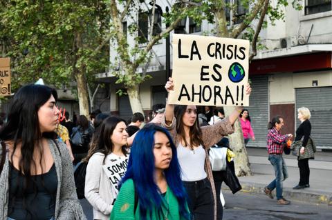 Una manifestación en la que varios jóvenes sostienen carteles, destacando uno que dice 'LA CRISIS ES AHORA!!'.