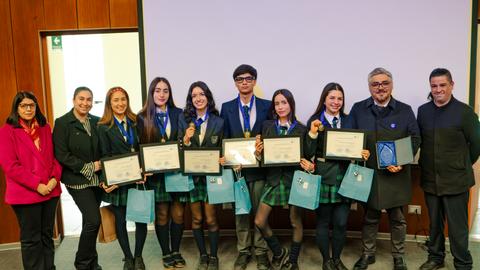 Un grupo de estudiantes sonrientes posando con sus certificados de reconocimiento en un evento escolar.