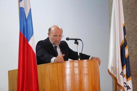 Un hombre se encuentra hablando en un podio con banderas chilenas a su lado.
