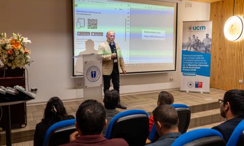 Un conferencista presenta información en una pantalla durante un evento en un auditorio.