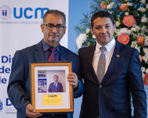 Dos hombres sostienen un marco con una foto en un evento de la Universidad Católica del Maule.