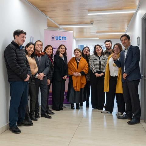 Un grupo de personas sonrientes posando en un pasillo con un banner de UCM al fondo.