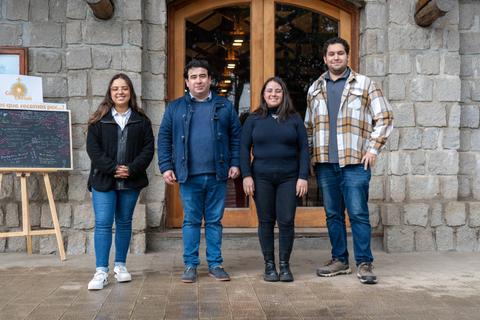 Cuatro personas posan frente a una entrada con una pared de piedra.