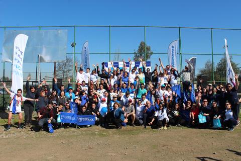 Un gran grupo de personas sonrientes se reúne al aire libre, levantando las manos en señal de celebración.