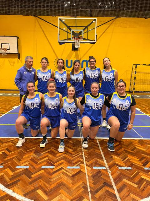 Un grupo de jugadoras de baloncesto posan en la cancha con su entrenador.