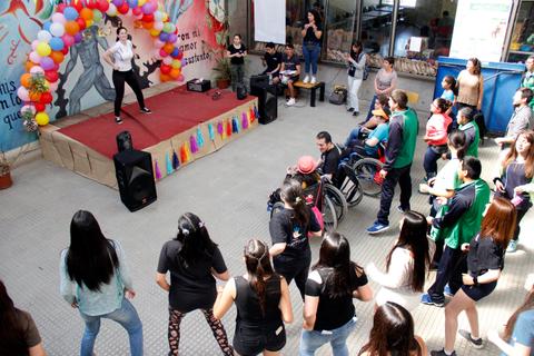 Un grupo de personas asiste a un evento en un espacio interior donde una mujer está bailando en un escenario decorado con globos.