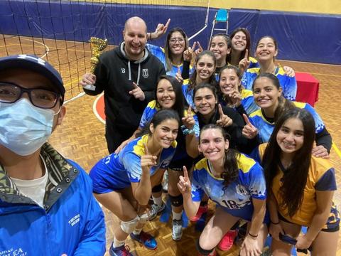 Un grupo de jugadoras de voleibol celebra su victoria junto a su entrenador en una cancha.
