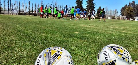 Un grupo de personas entrena en un campo de fútbol mientras dos balones reposan en primer plano.