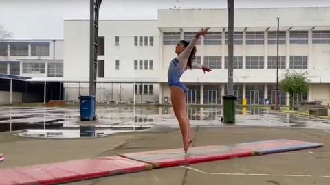Una gimnasta realiza un salto sobre una superficie de entrenamiento en un día lluvioso.