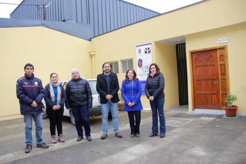 Seis personas posan frente a un edificio amarillo en un día nublado.