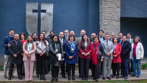 Un grupo de personas posando en una reunión organizada frente a un fondo con una cruz.