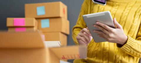 Una persona utilizando una tablet mientras está rodeada de cajas de cartón.