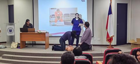 Un grupo de personas participa en una demostración de primeros auxilios en un aula.
