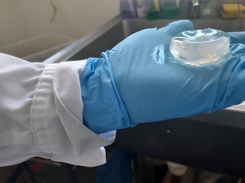 Una mano con un guante azul sostiene un objeto transparente que parece gel.