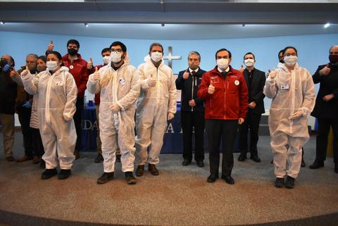 Grupo de personas en un evento, todas con mascarillas y algunos con trajes de protección, mostrando el pulgar hacia arriba.
