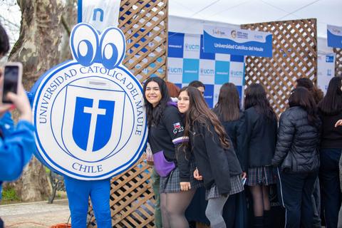 Un grupo de estudiantes posando con una figura del logo de la Universidad Católica del Maule en un evento al aire libre.