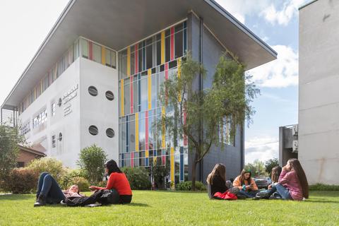 Un grupo de personas se reúne en un jardín frente a un edificio moderno y colorido.