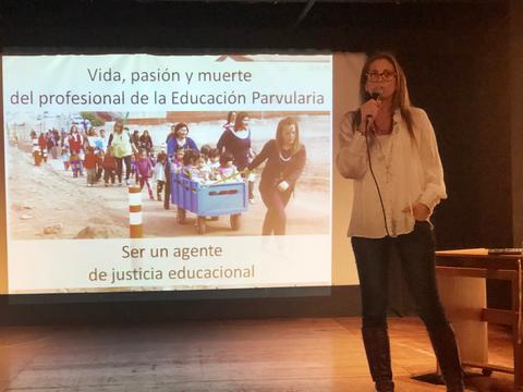 Una mujer habla frente a una presentación sobre la educación parvularia mientras se muestra una imagen de niños y educadores en una actividad al aire libre.