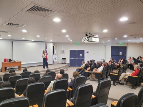 Una presentación en una sala con público sentado y un docente hablando.