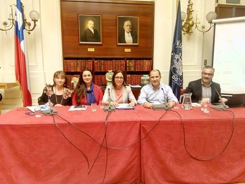 Cinco personas sentadas en una mesa durante un evento formal en un salón con retratos en la pared.